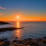 Éclipse solaire partielle au coucher du Soleil au-dessus de l’océan Atlantique, vue depuis une côte rocheuse française.