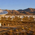Grand réseau d’antennes radio blanches installé dans un désert du Nevada, avec des ingénieurs au pied d’une parabole géante.