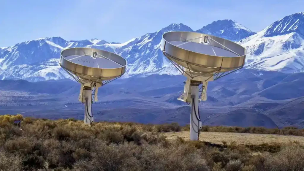 Deux antennes paraboliques du Deep Synoptic Array installées dans le désert du Nevada devant une chaîne de montagnes enneigées.