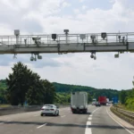 Ancien portique écotaxe équipé de caméras au-dessus d’une route française avec des voitures et camions en circulation.