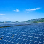 Immense champ de panneaux solaires en Chine sous un ciel bleu, avec des montagnes en arrière-plan.