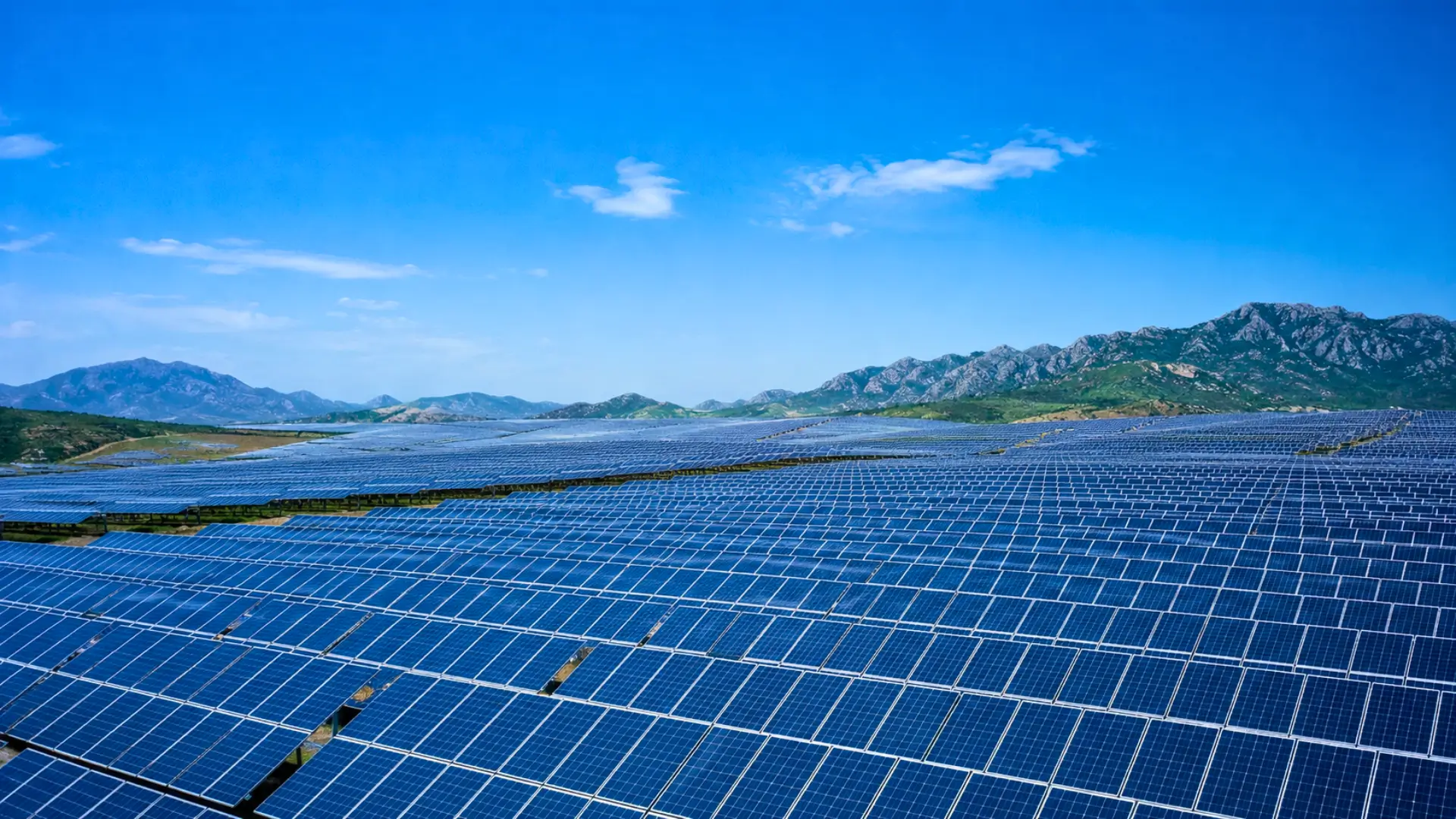 Immense champ de panneaux solaires en Chine sous un ciel bleu, avec des montagnes en arrière-plan.