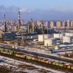 Complexe industriel russe enneigé avec raffinerie, réservoirs de carburant, cheminées, voies ferrées et immeubles urbains en arrière-plan.