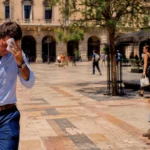 Homme transpirant dans une place européenne en plein soleil pendant une forte vague de chaleur estivale.