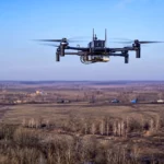 Drone quadricoptère de communication volant au-dessus d’un paysage de front ukrainien, avec des véhicules militaires visibles au loin.