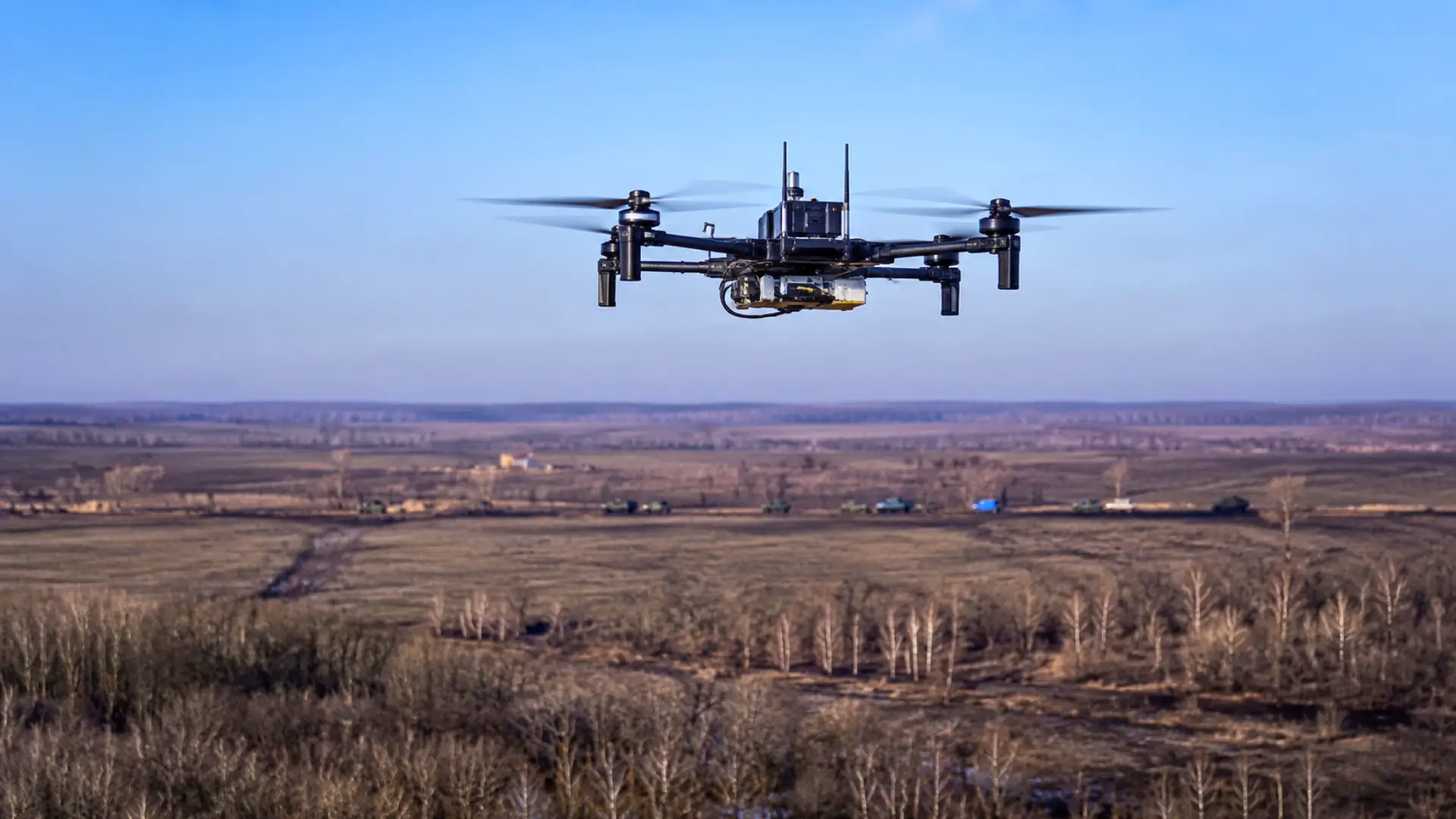 Drone quadricoptère de communication volant au-dessus d’un paysage de front ukrainien, avec des véhicules militaires visibles au loin.