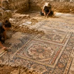 Mosaïque romaine polychrome dégagée dans une tranchée archéologique en terre.