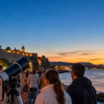 Public observant la Lune au télescope sur une promenade côtière au crépuscule.