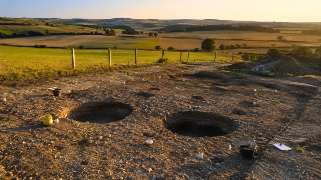 Site archéologique dans la campagne du Wiltshire montrant deux grands trous de poteaux découverts près de Stonehenge au coucher du soleil.