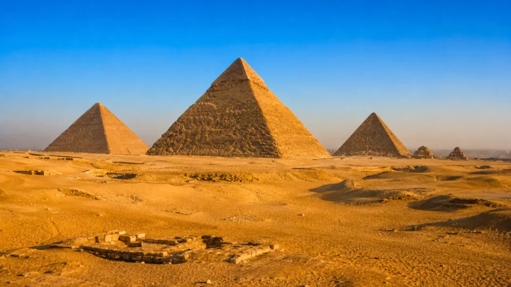 Vue panoramique des pyramides de Gizeh dans le désert, avec la Grande Pyramide de Khéops au centre sous une lumière dorée