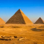 Vue panoramique des pyramides de Gizeh dans le désert, avec la Grande Pyramide de Khéops au centre sous une lumière dorée
