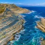 Vue aérienne réaliste de falaises calcaires striées en bord de Méditerranée, évoquant les traces géologiques d’un ancien mégaflot.