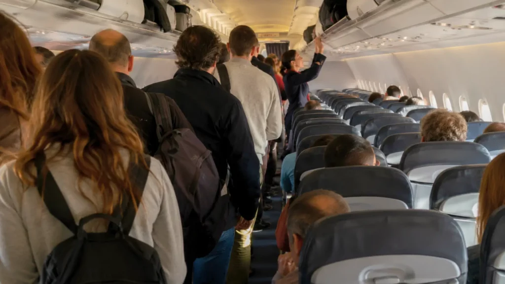 Passagers embarquant dans un avion, certains rangeant leurs bagages cabine dans les coffres au-dessus des sièges.