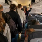 Passagers embarquant dans un avion, certains rangeant leurs bagages cabine dans les coffres au-dessus des sièges.