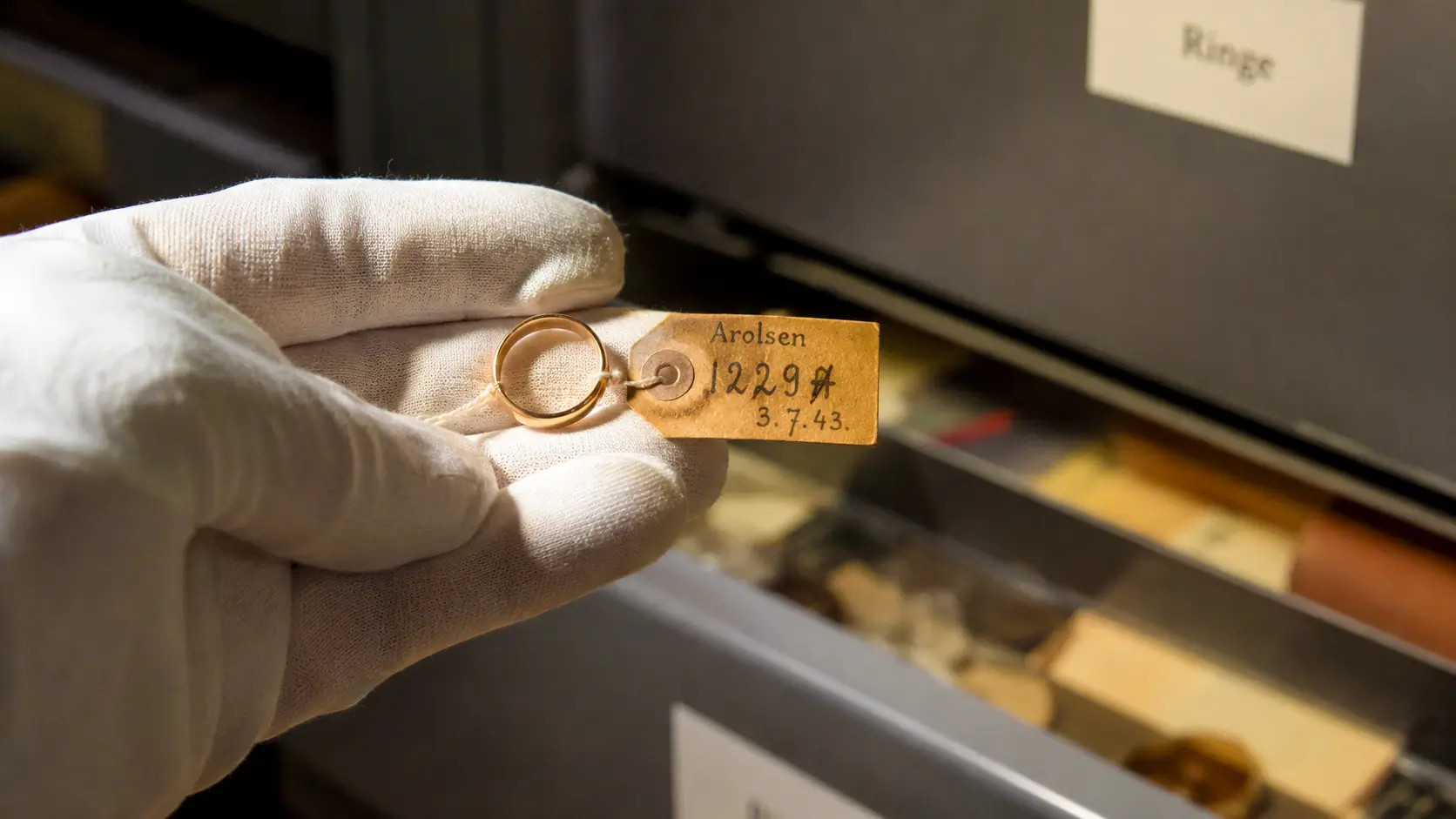 Une alliance confisquée à un déporté est manipulée avec précaution par un archiviste aux Arolsen Archives en Allemagne.