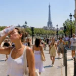 Jeune femme se rafraîchissant avec une bouteille d’eau lors d’une journée de canicule à Paris, près de la tour Eiffel.