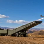 Une catapulte électromagnétique mobile montée sur camions lance un drone militaire depuis un plateau désertique montagneux.