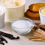 Desserts à la vanille, gousses naturelles, cristaux de vanilline et morceaux de bois illustrant les différentes origines de l’arôme vanille.