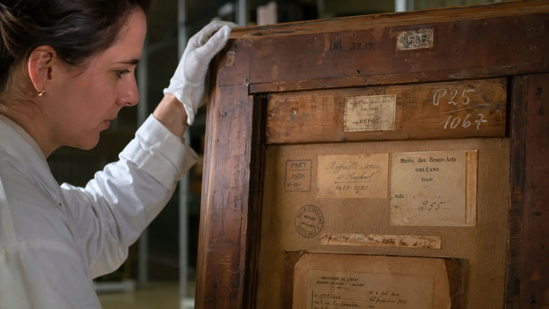 Une conservatrice examine les anciennes étiquettes et inscriptions au dos d’un tableau recherché par le musée des Beaux-Arts d’Orléans.