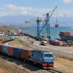 Un train de marchandises chargé de conteneurs arrive dans un port de la mer Caspienne, où des grues transfèrent le fret vers un navire.