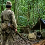 Soldat japonais vu de dos dans la jungle de Lubang, près d’un campement de fortune, tenant un fusil.