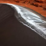 Une immense dune sombre du cratère Kaiser sur Mars, dont la crête recouverte de givre de dioxyde de carbone semble briller comme du chrome liquide.