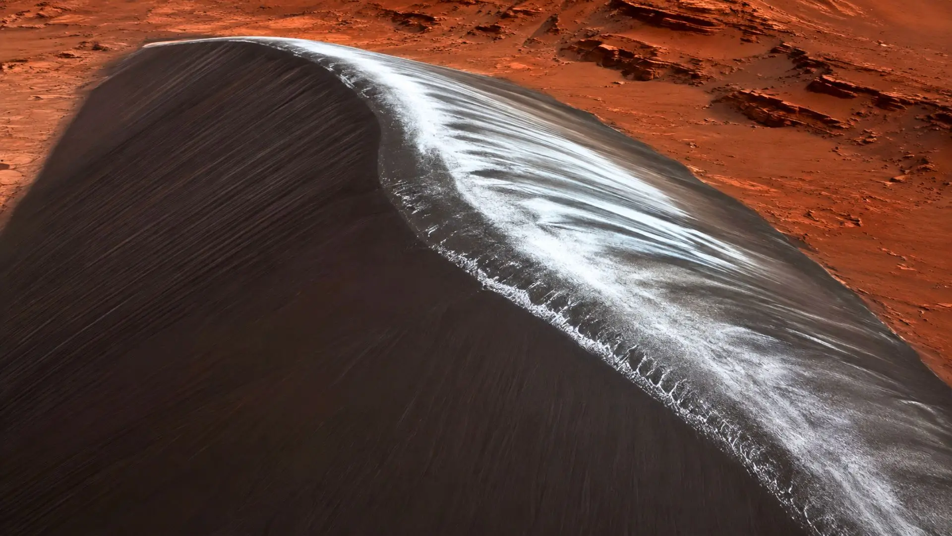 Une immense dune sombre du cratère Kaiser sur Mars, dont la crête recouverte de givre de dioxyde de carbone semble briller comme du chrome liquide.
