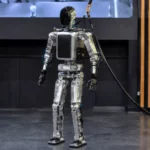 Robot humanoïde français Northstar debout dans un espace de démonstration, relié à un câble d’alimentation et à un harnais de sécurité.