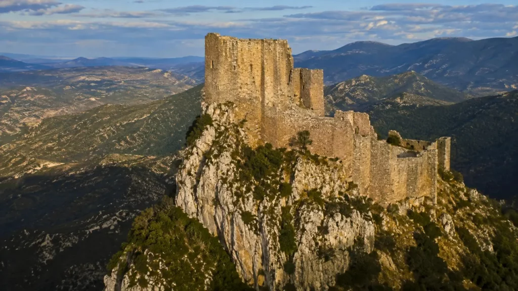 Une forteresse médiévale en ruines domine un éperon rocheux du Languedoc, au cœur d’un paysage montagneux.