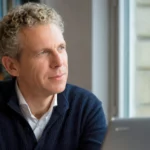 Gilles Babinet observe la lumière depuis son bureau, assis devant un ordinateur portable, dans un moment de réflexion sur l’intelligence artificielle.