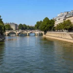 Vue réaliste de la Seine à Paris en été, avec un niveau d’eau légèrement réduit, des quais en pierre, des arbres et un pont parisien.