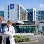 Deux responsables consultent des plans devant le Centre hospitalier Sud Francilien, symbole des surcoûts et des malfaçons du partenariat public-privé.