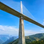 Grand viaduc à haubans dominant une vallée verdoyante, avec de très hautes piles en béton sous un ciel bleu.