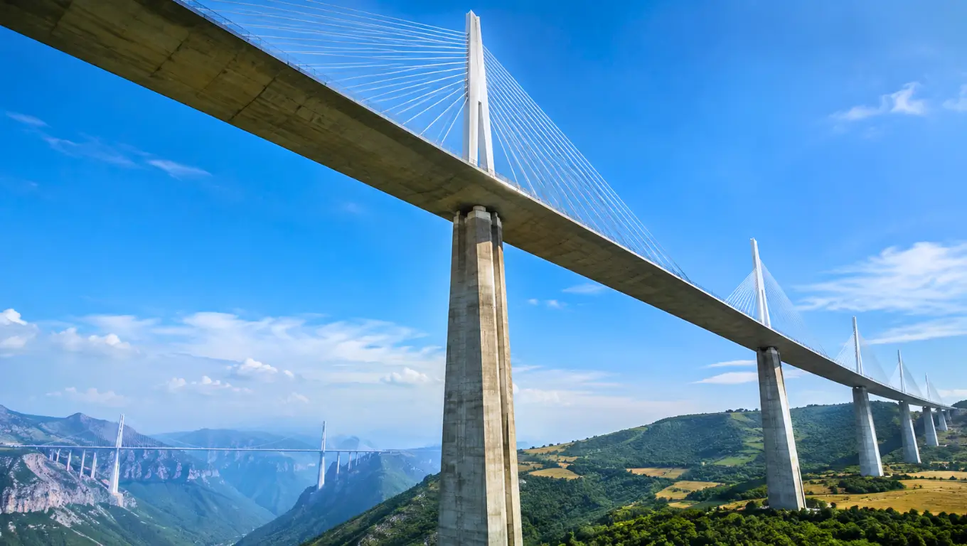 Grand viaduc à haubans dominant une vallée verdoyante, avec de très hautes piles en béton sous un ciel bleu.