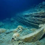 Épave grecque antique reposant sur le fond marin au large de Cannes, entourée d’amphores et de vestiges de coque en bois.