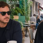 Homme portant des lunettes connectées avec voyant d’enregistrement dans un café, observé par une femme assise à proximité.