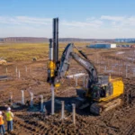 Robot de chantier autonome installant des pieux métalliques sur une ferme solaire en construction en Louisiane, avec un data center Meta en arrière-plan.