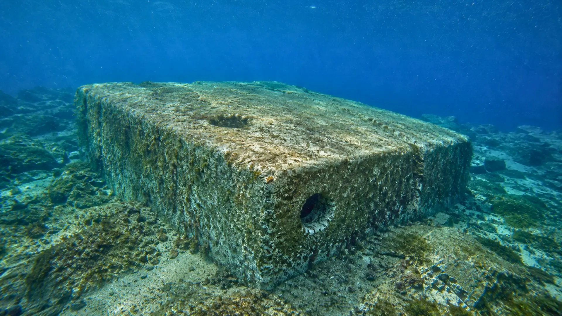 Un imposant monolithe préhistorique percé de cavités repose sur le fond marin dans les eaux bleues du canal de Sicile.