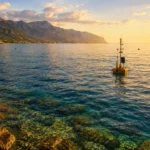 Bouées scientifiques flottant sur une mer Méditerranée calme et anormalement chaude au coucher du soleil, près d’une côte rocheuse.