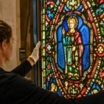 Une conservatrice gantée examine un vitrail médiéval aux couleurs éclatantes dans la Cité du Vitrail à Troyes.