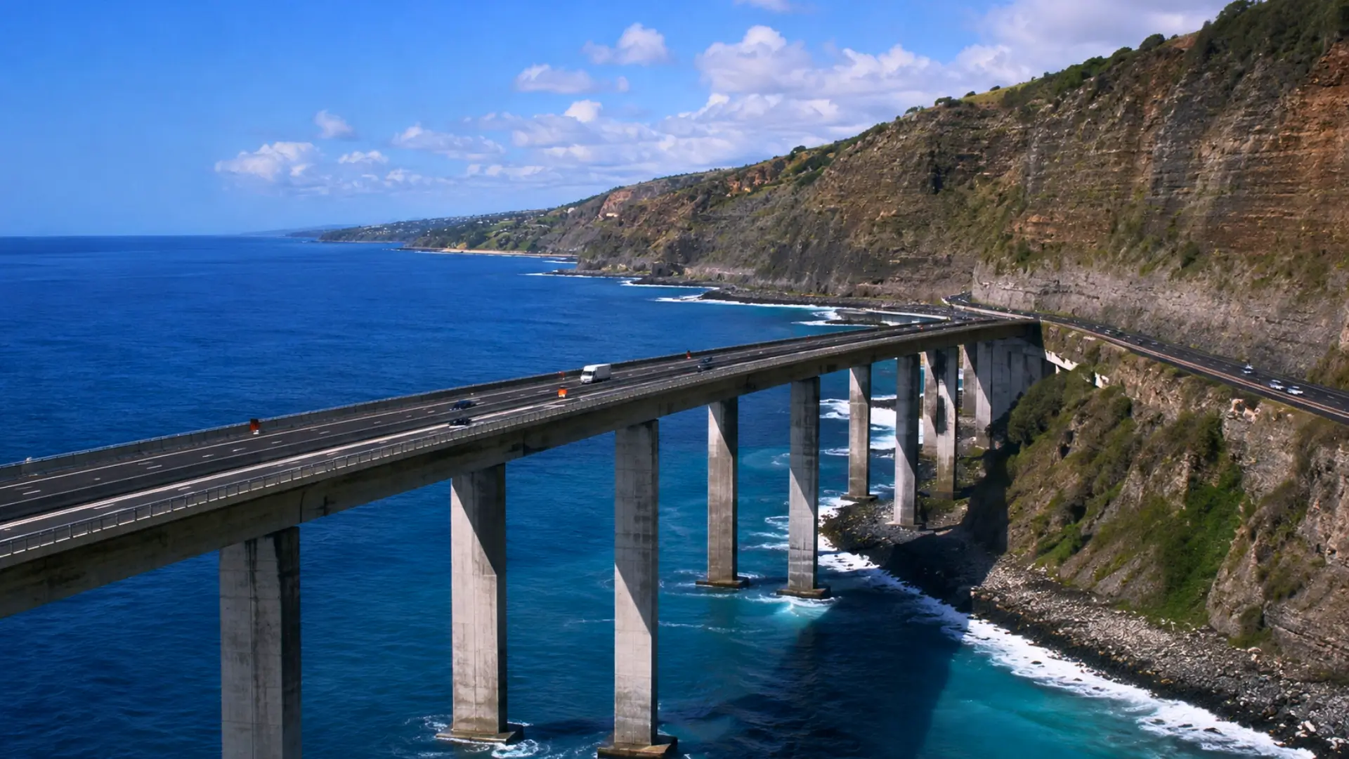 Vue aérienne du viaduc de la Nouvelle Route du Littoral à La Réunion, longeant l’océan Indien avant de rejoindre l’ancienne route au pied des falaises.