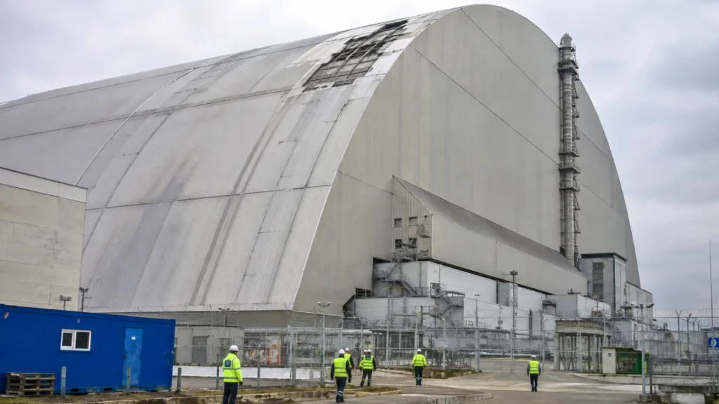 Vue extérieure de l’arche de confinement de Tchernobyl protégeant le réacteur 4, avec des équipes techniques au pied de la structure.