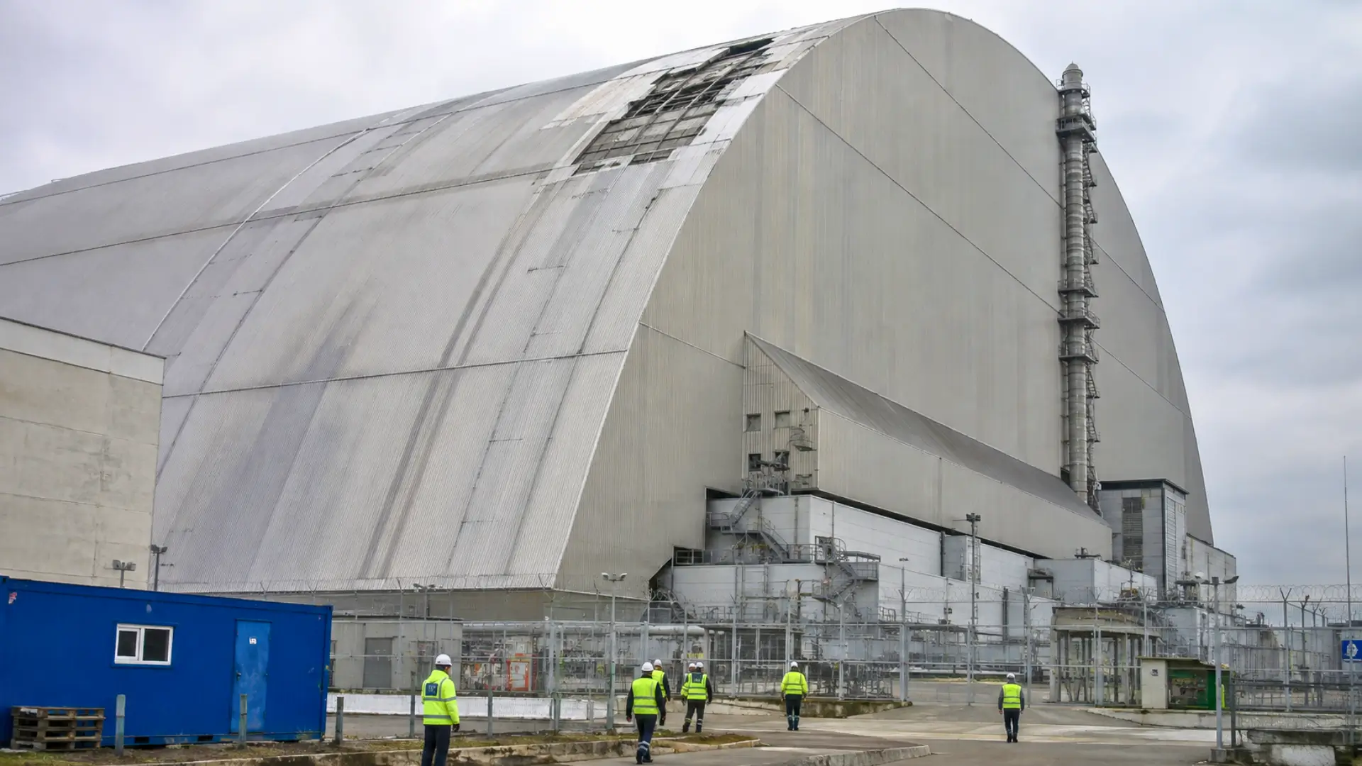 Vue extérieure de l’arche de confinement de Tchernobyl protégeant le réacteur 4, avec des équipes techniques au pied de la structure.