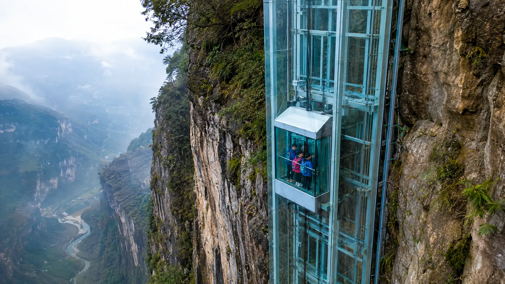 Un ascenseur géant en verre longe une falaise vertigineuse dans le canyon brumeux de Nizhuhe, au Yunnan, avec des écoliers à bord.