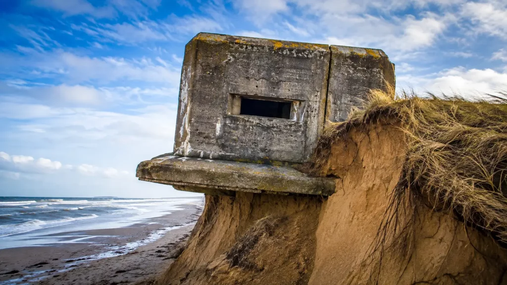 Un bunker du mur de l’Atlantique surplombe une dune fortement érodée, tandis que le sable disparaît sous sa fondation en béton.