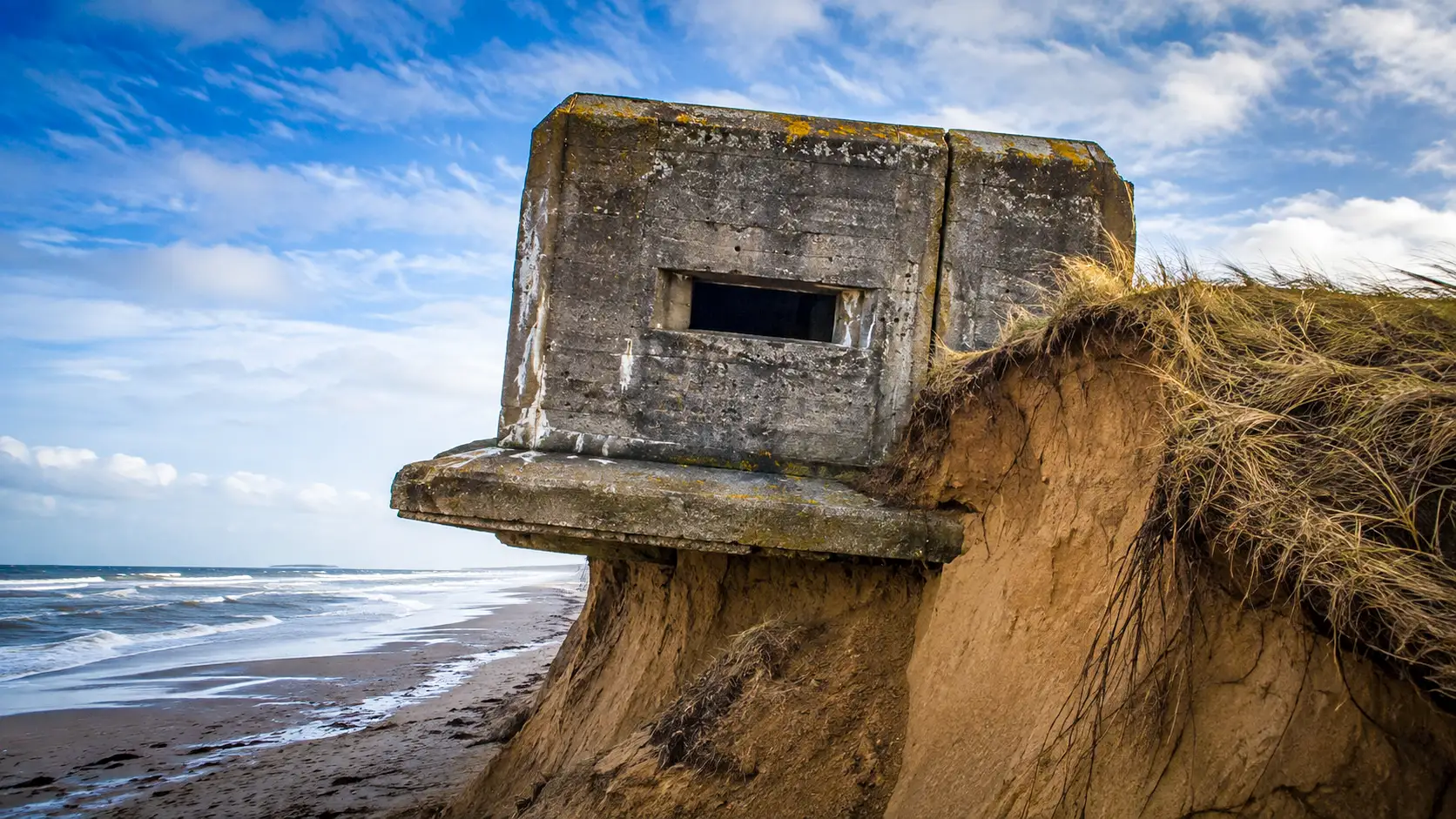 Un bunker du mur de l’Atlantique surplombe une dune fortement érodée, tandis que le sable disparaît sous sa fondation en béton.