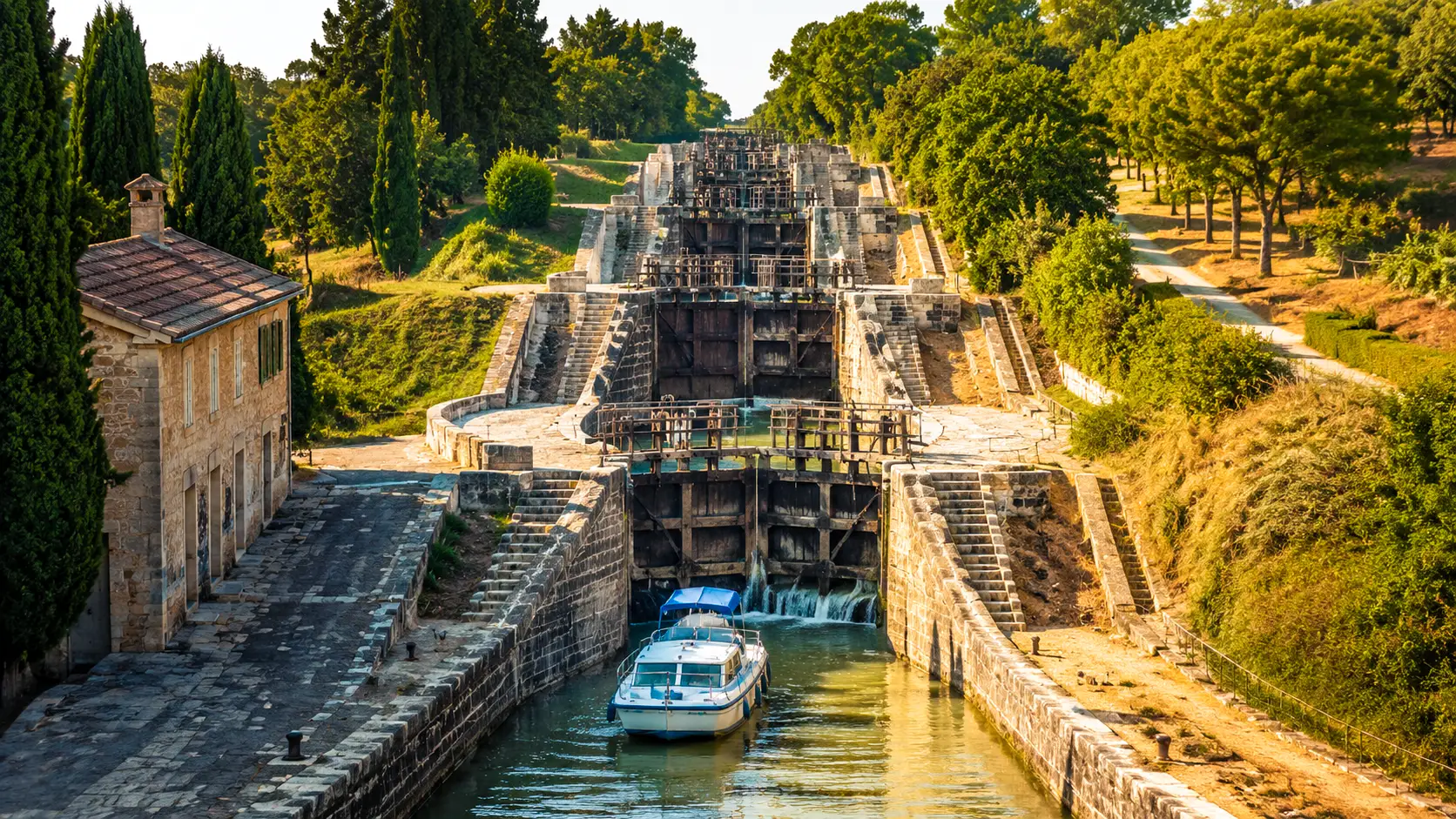 Vue sur les écluses historiques du Canal du Midi, avec une embarcation naviguant entre les bassins de pierre entourés de végétation.