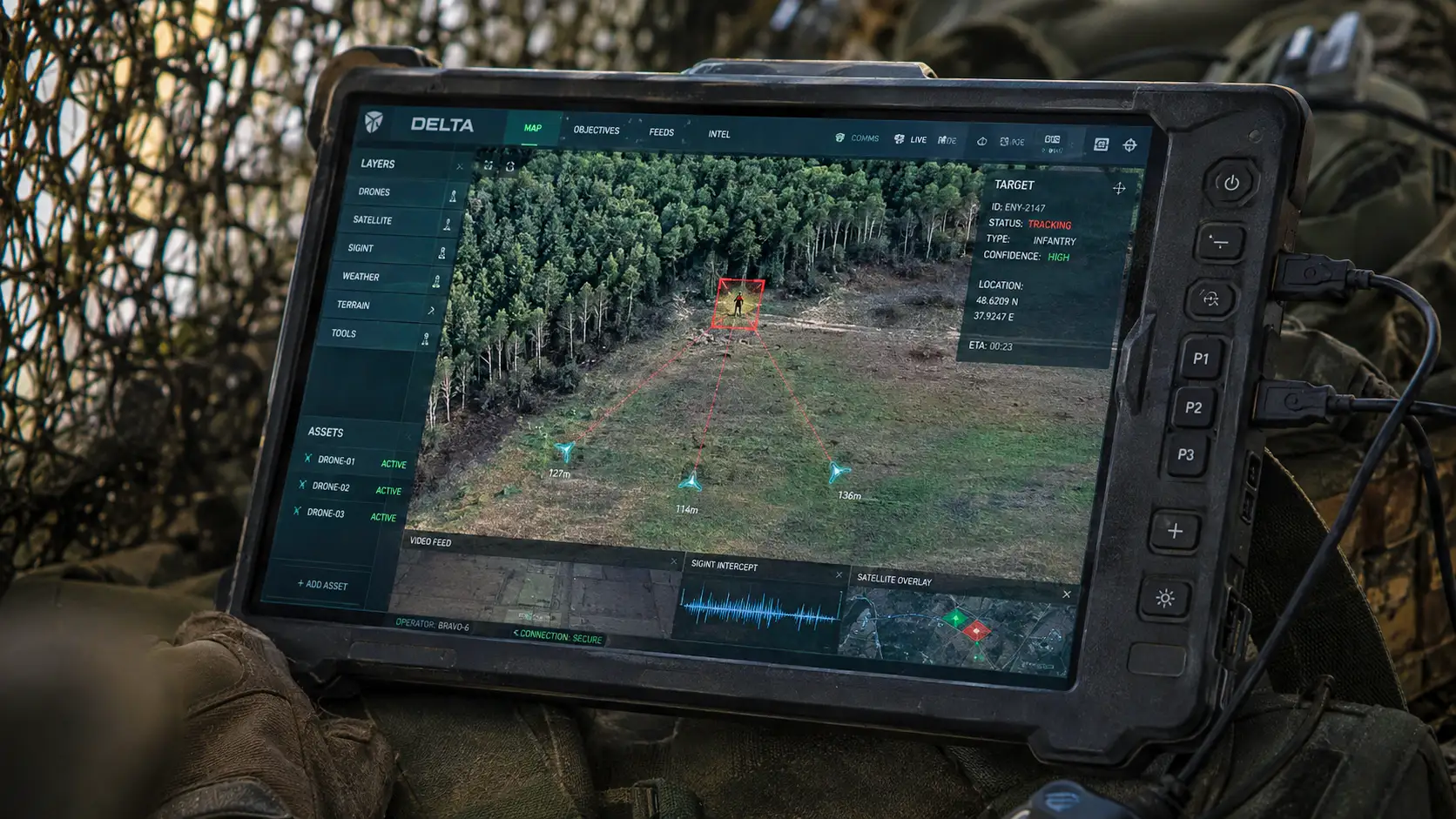 Une tablette militaire affiche l’interface Delta avec une cible encadrée en rouge et trois drones convergeant vers sa position.