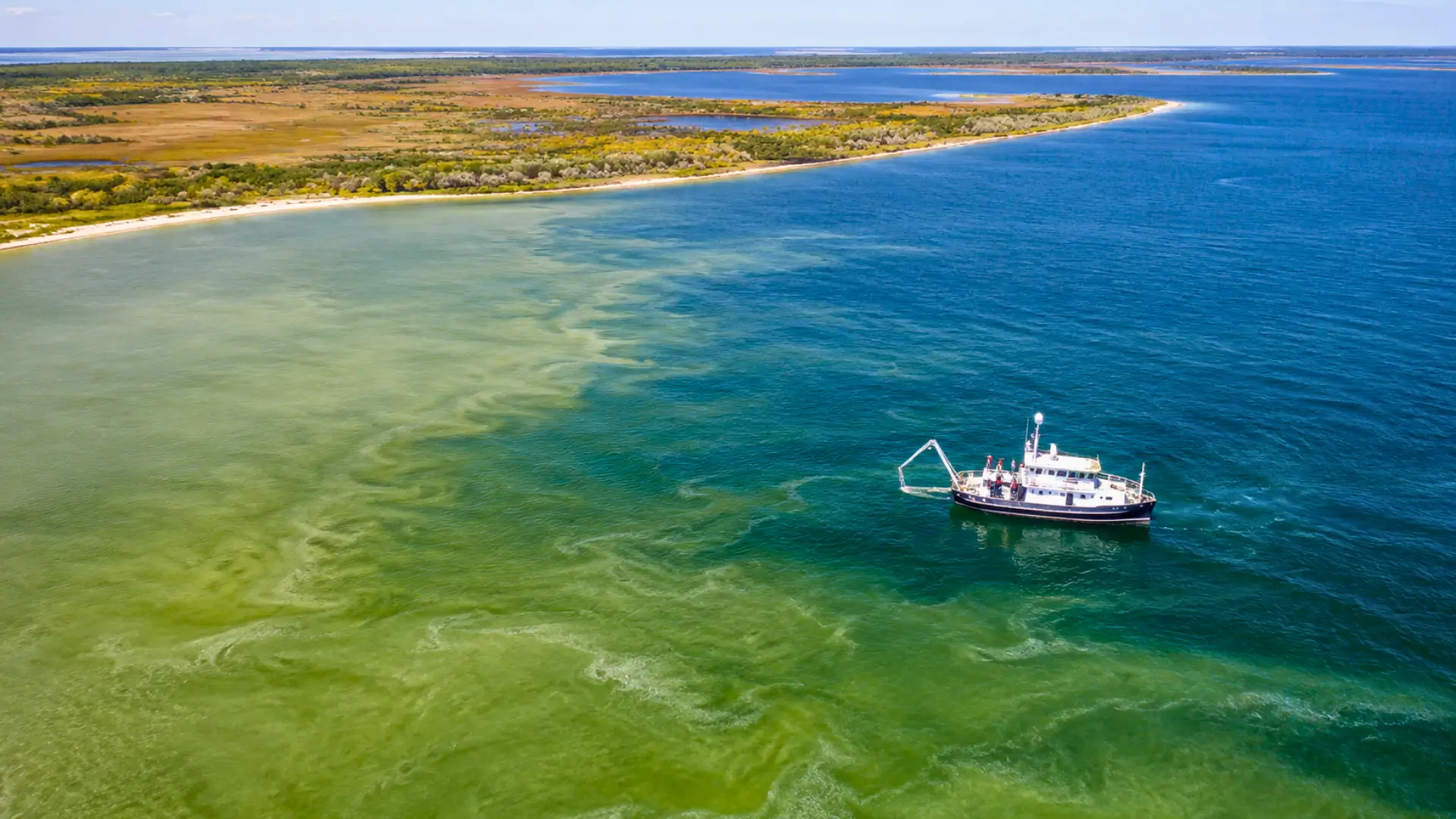 Vue aérienne du littoral de la mer Noire montrant des eaux verdâtres liées à une prolifération de phytoplancton près d’un navire scientifique.