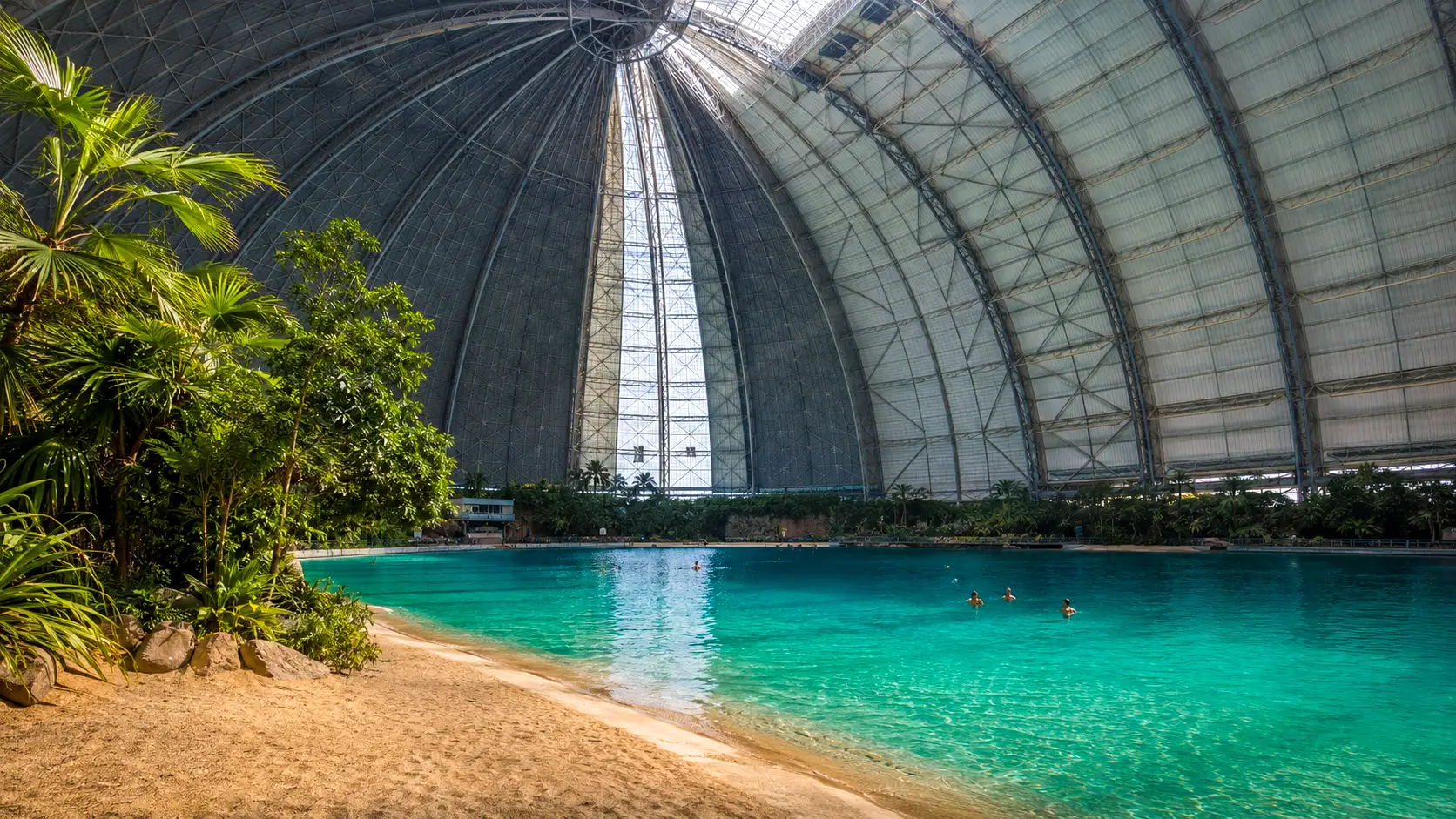 Un immense lagon tropical aux eaux turquoise s’étend sous la structure métallique monumentale d’un ancien hangar à dirigeables près de Berlin.